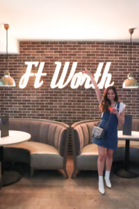alexandria holding a drink standing in front of a fort worth sign